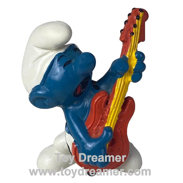 Smurf figurine playing a red and yellow guitar with 'Toy Dreamer' branding.